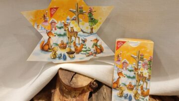 Adventskalender-Tee in Sternform und normaler rechteckiger Verpackung dekoriert auf einem weißen Tuch mit Holzstämmen.