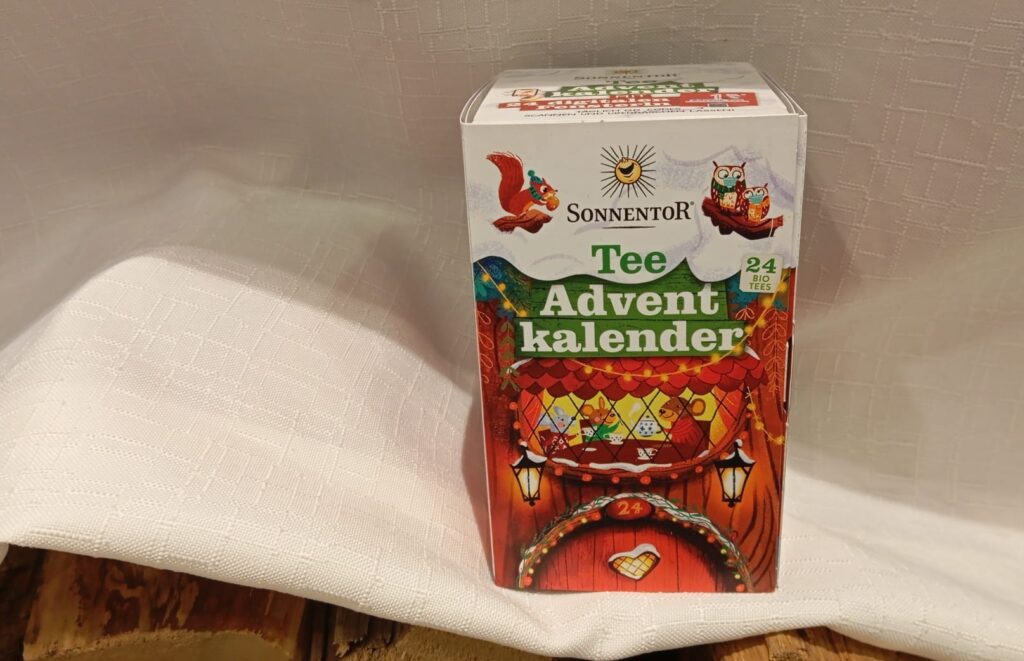 Adventskalender Tee von Sonnentor dekoriert auf weißem Tuch mit Holz.