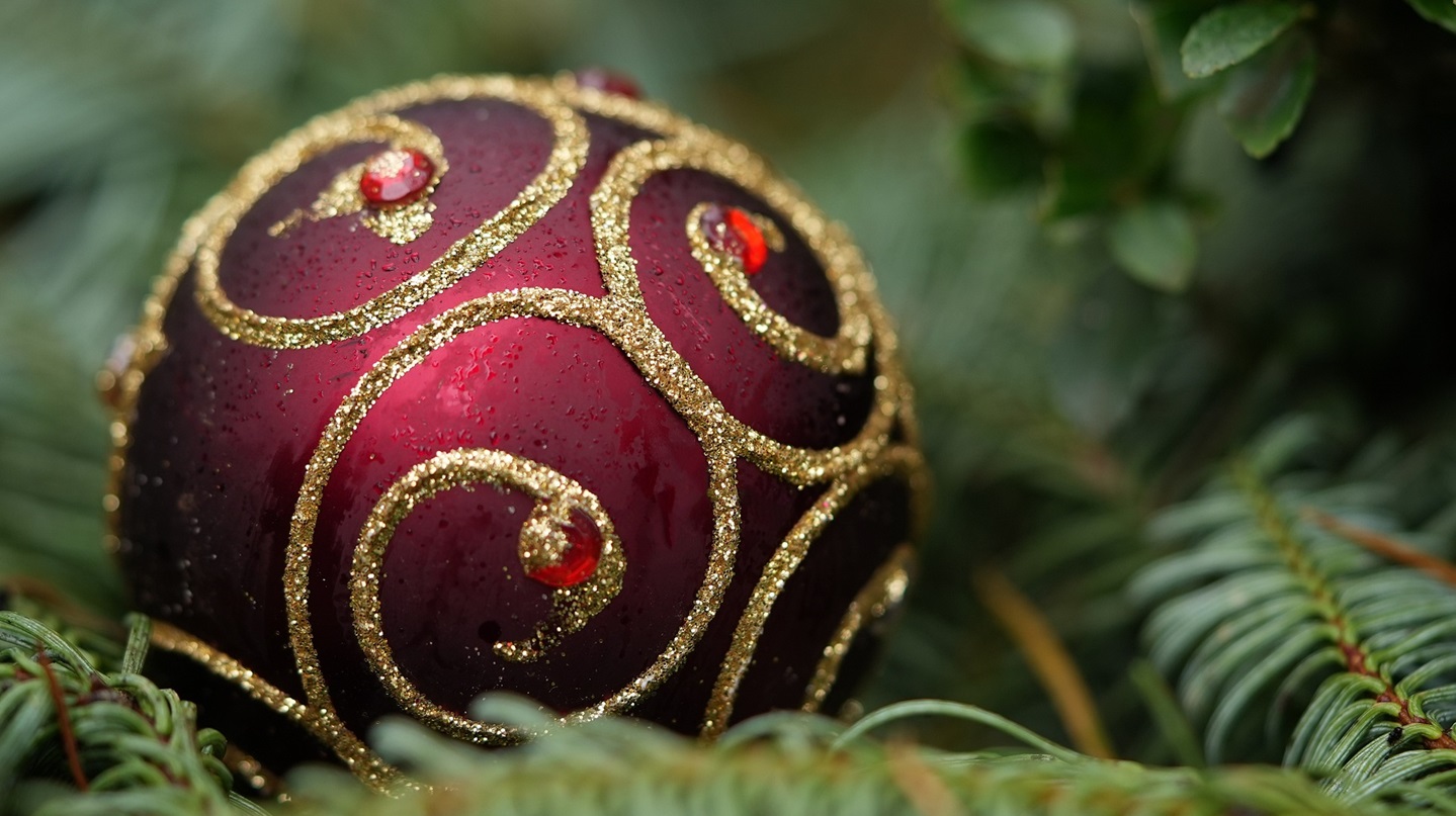 Mit goldenen Streifen verzierte Weihnachtskugel auf Tannenzweigen